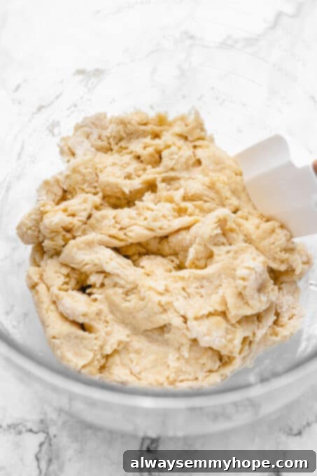 Ingredients for vegan dinner rolls stirred into a shaggy dough ball, showing initial mixing consistency.