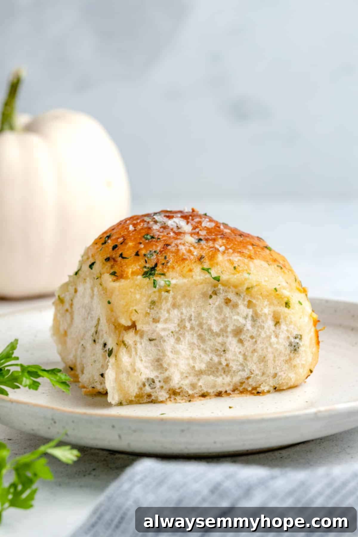 Fluffy Vegan Garlic Parmesan Dinner Rolls 16 Single garlic dinner roll on a plate with a white pumpkin in the background