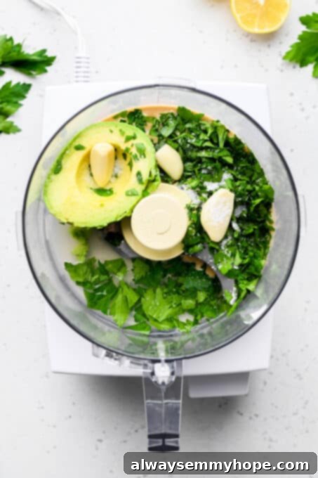 Divine Green Pasta 5 Fresh ingredients for green goddess sauce, including avocado, parsley, lemon, tahini, and garlic, placed in a food processor bowl before blending.