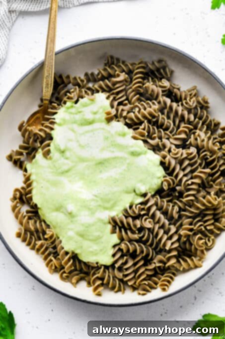 Divine Green Pasta 7 A rich, green goddess sauce being poured over freshly cooked lentil pasta in a pan, ready to be mixed for a creamy dish.