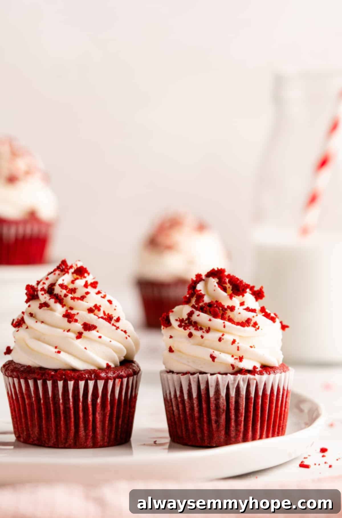 Two exquisitely frosted vegan red velvet cupcakes, featuring impressive peaks of vegan cream cheese frosting and a scattering of fine cake crumbs, highlighting their bakery-style appeal.