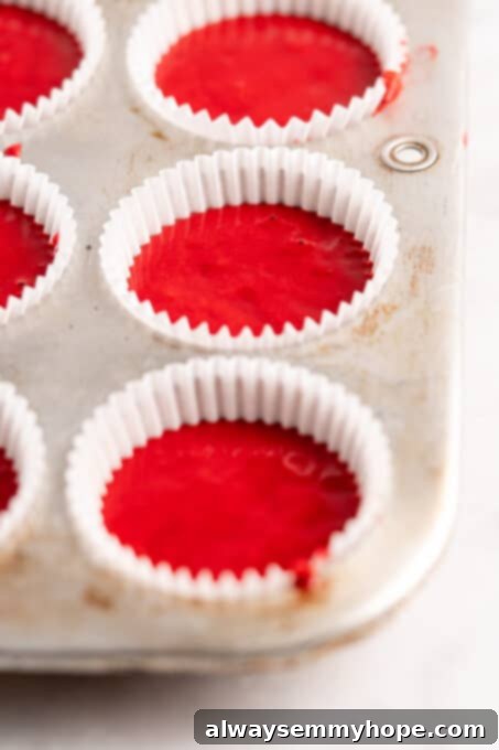 A closer look at a cupcake tin filled with vibrant red velvet cake batter in liners, just before being placed into the oven, showcasing the even distribution of batter.