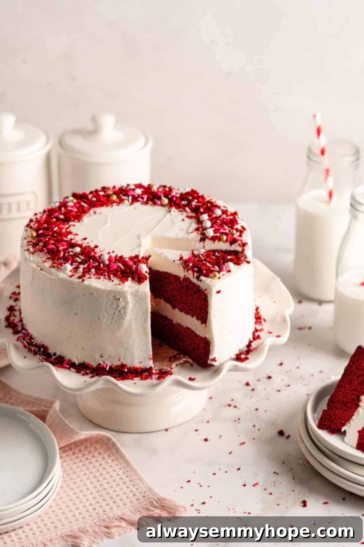 A stunning vegan red velvet cake displayed on an elegant cake stand, with a slice being removed, revealing its moist red layers and creamy white frosting.