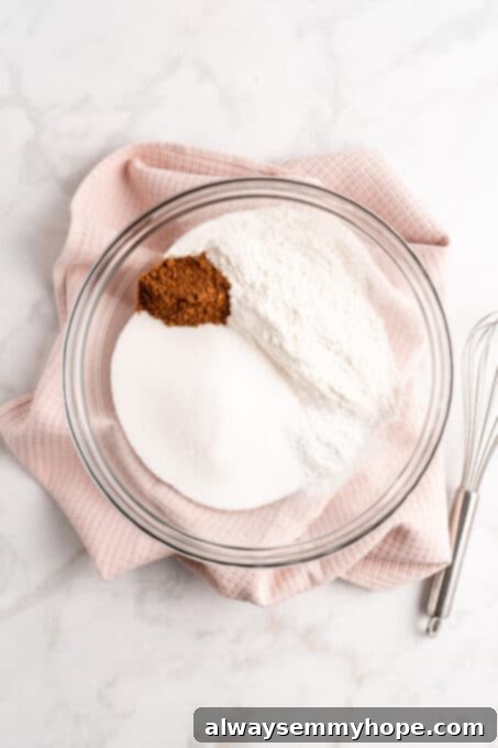 Overhead view of cocoa powder, sugar, and flour in a clear glass mixing bowl, ready to be combined for the cake batter.