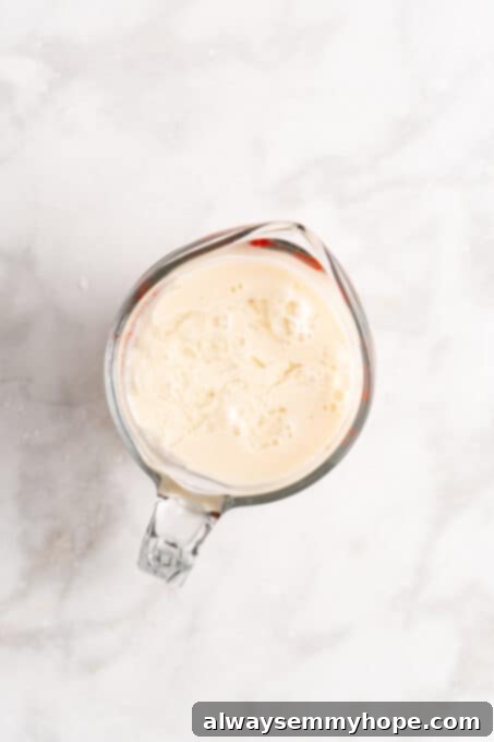 Overhead view of wet ingredients for the cake, including oil, vegan buttermilk, vanilla extract, and red food coloring, in a glass measuring cup.