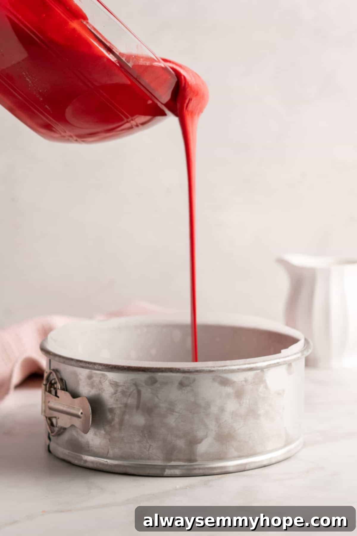 Close-up shot of vibrant red vegan red velvet cake batter being poured into a parchment-lined cake pan, ready for baking.