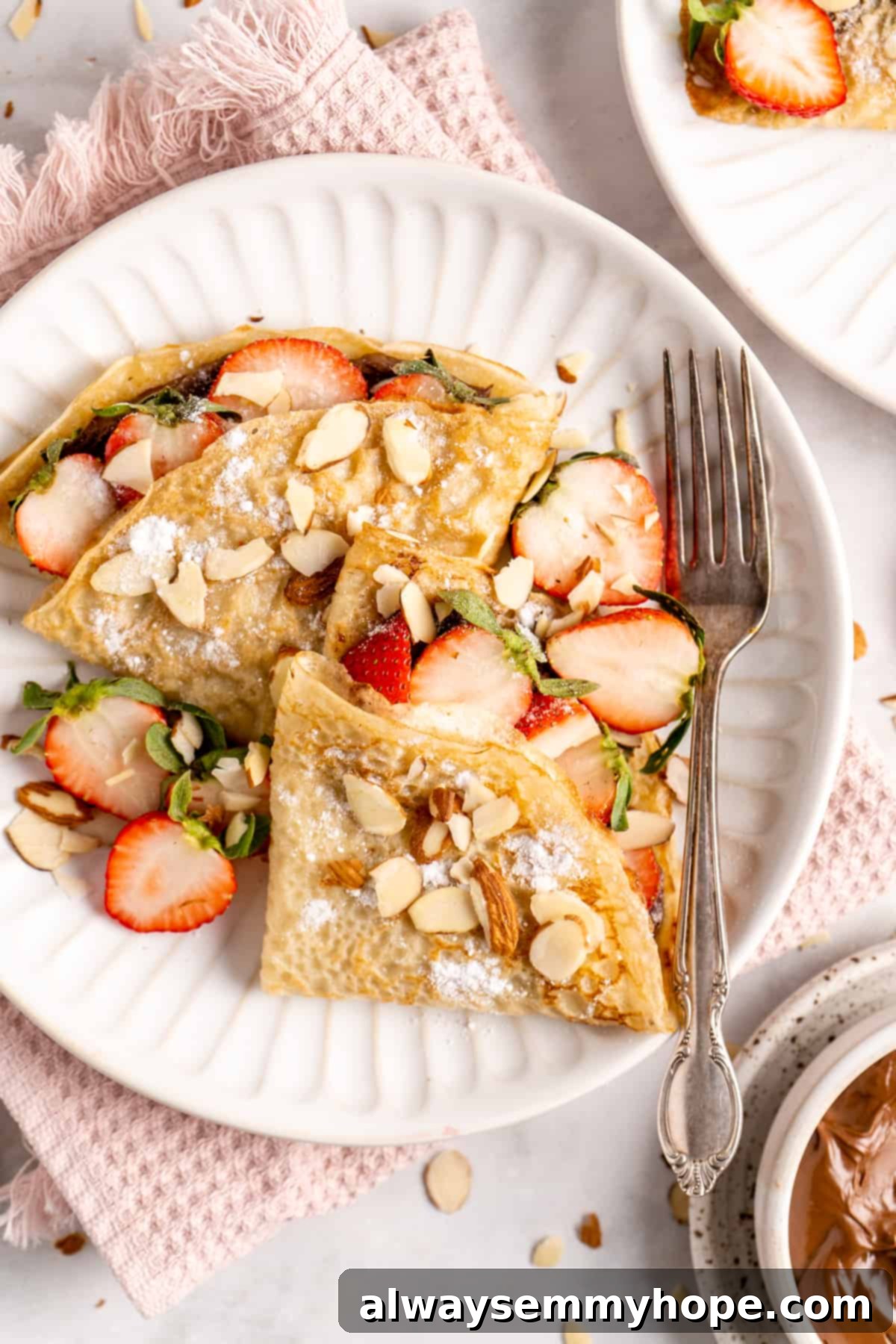 crepes on a plate with a fork with strawberries and almonds on top