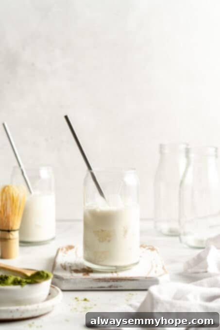 Smooth Iced Matcha Latte 11 Two clear glass tumblers with ice cubes, now filled with creamy plant-based milk, creating a layered effect.