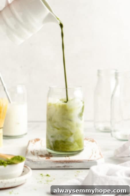 Smooth Iced Matcha Latte 12 The vibrant green matcha mixture being poured over ice and plant milk in a glass tumbler, forming a beautiful two-toned drink.