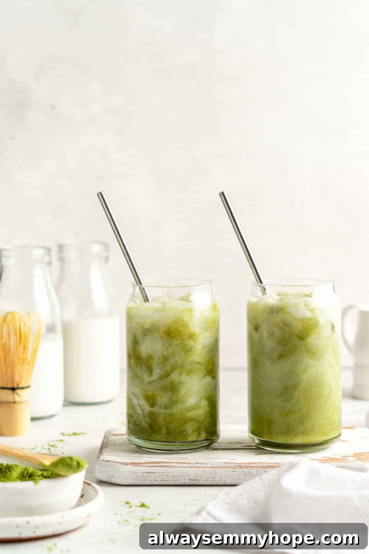 Smooth Iced Matcha Latte 14 Two iced matcha lattes in clear glass tumblers with stainless steel straws, showing distinct swirls of green matcha and creamy white milk.