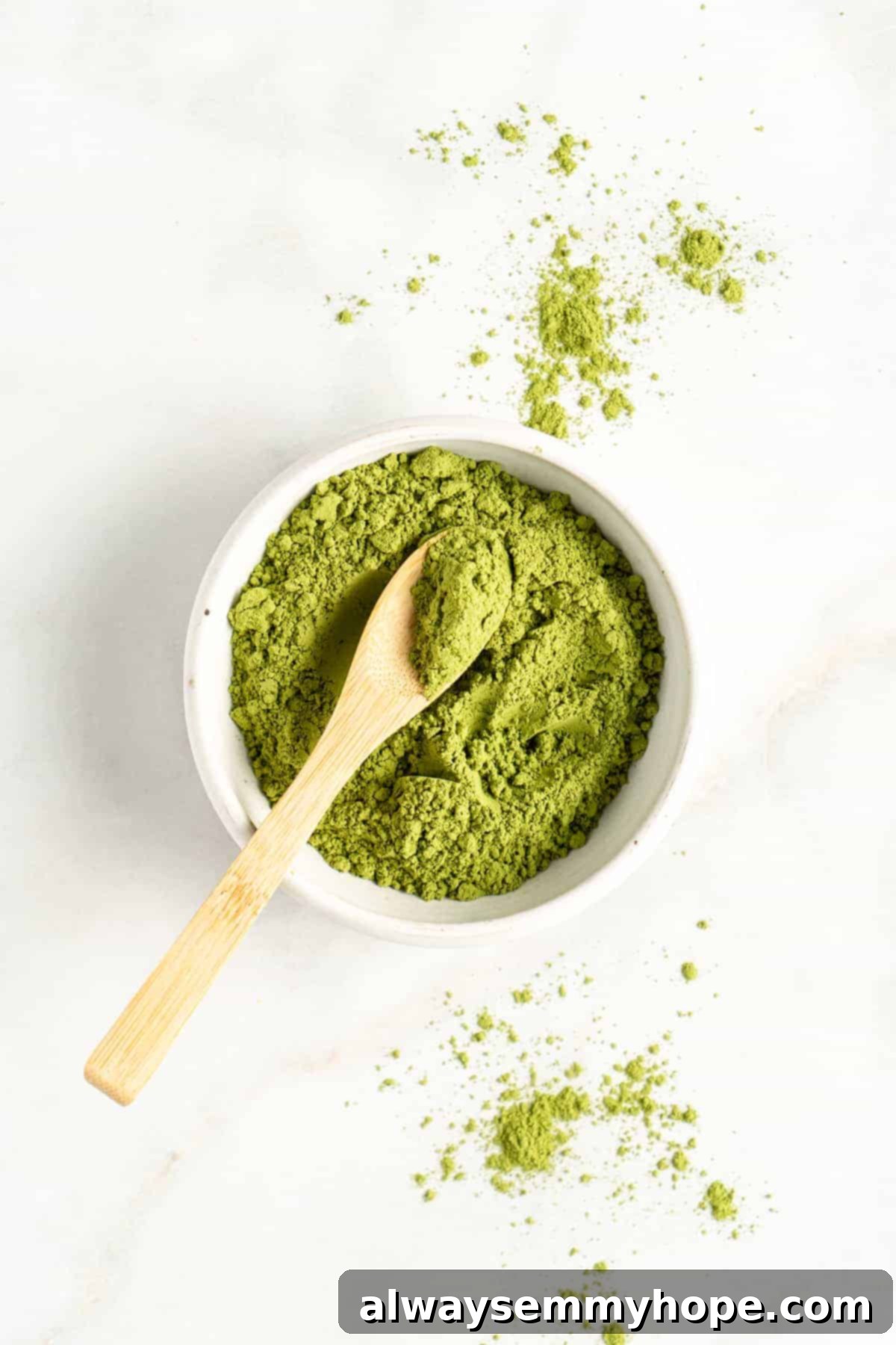 Smooth Iced Matcha Latte 4 Small bowl of bright green matcha powder with a delicate wooden chashaku (matcha scoop) resting on the side.