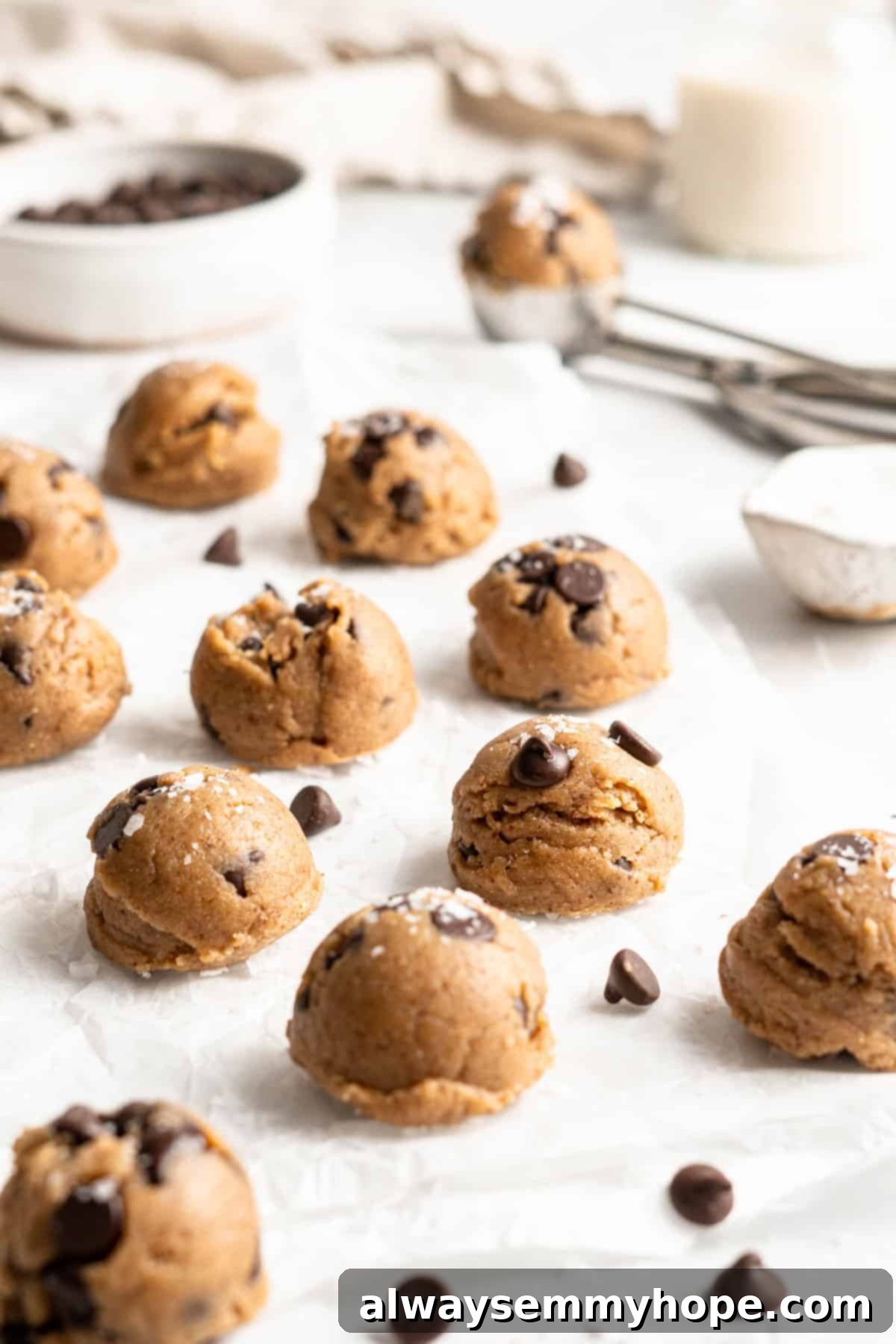 Vegan cookie dough balls on parchment paper with chocolate chips scattered between