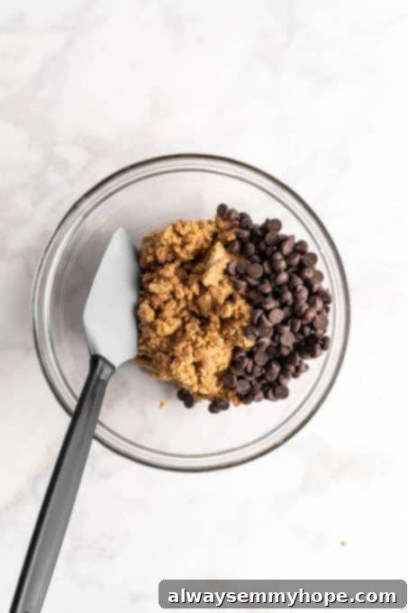 Overhead view of cookie dough and chocolate chips in glass bowl with spatula
