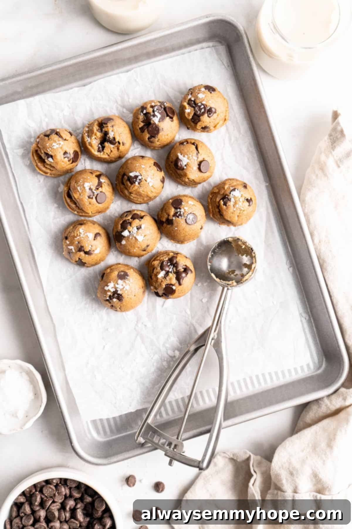 Overhead view of edible cookie dough balls on baking sheet with cookie dough scoop
