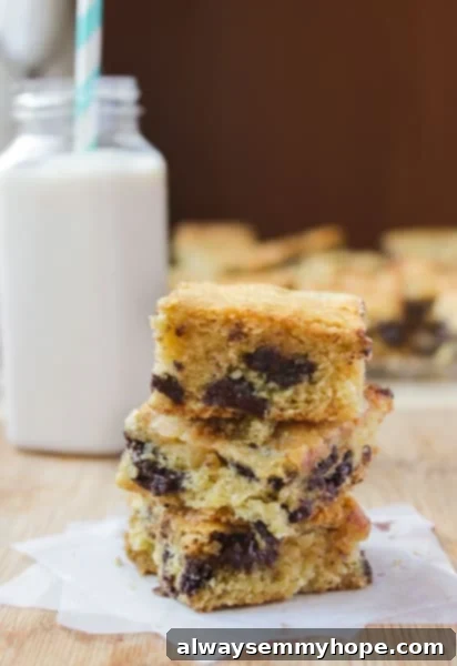 These Ghirardelli Chocolate Chip Cookie Bars were ah-mazing. Made with cream cheese and dark chocolate chips, they melt right in your mouth. Stack of Chocolate Chip Cookie Bars with a glass of milk in the background.