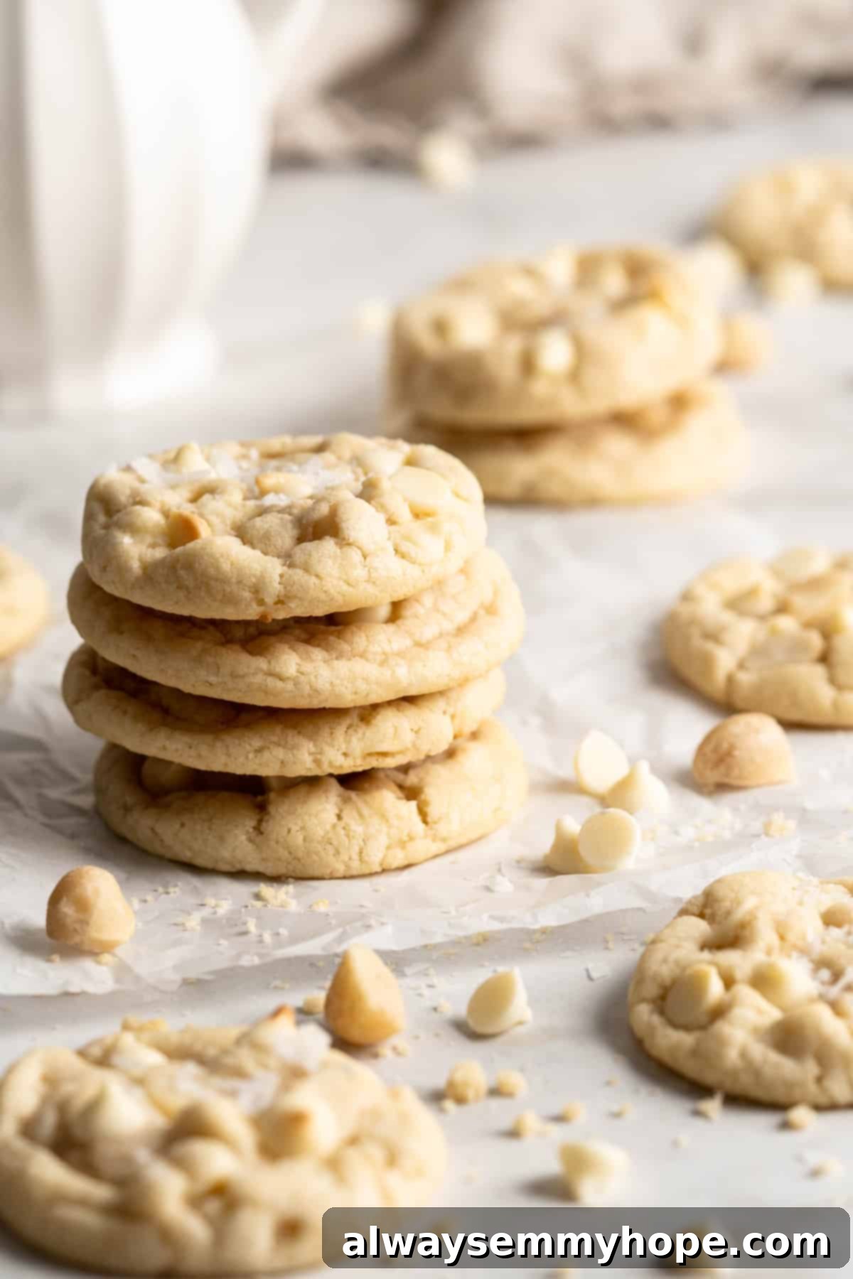 Freshly baked vegan white chocolate macadamia nut cookies, a perfect treat. Stacks of warm vegan white chocolate macadamia nut cookies artfully arranged on a countertop, surrounded by scattered white chocolate chips for a tempting display.