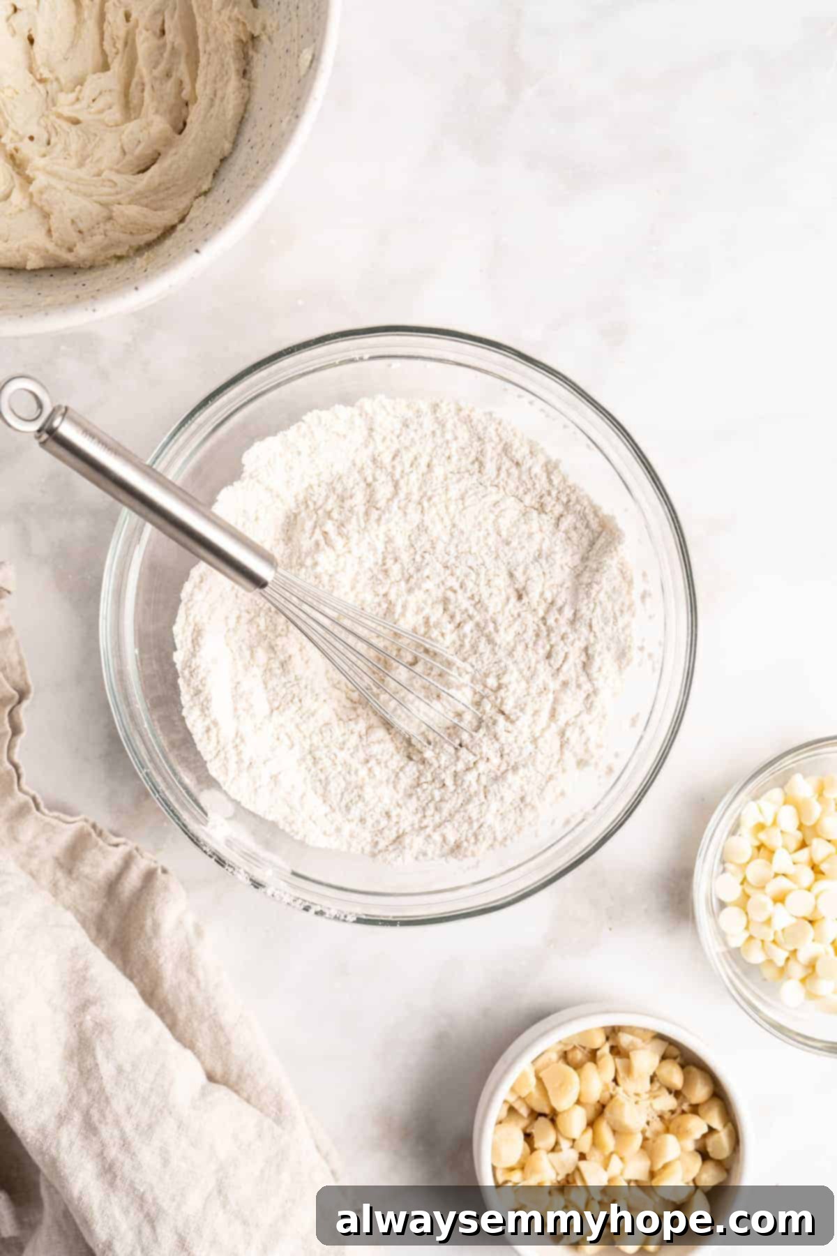 Dry ingredients for vegan cookies, perfectly whisked. Overhead view of dry cookie dough ingredients — flour, cornstarch, baking soda, and sea salt — perfectly combined in a glass bowl, awaiting the wet mixture.