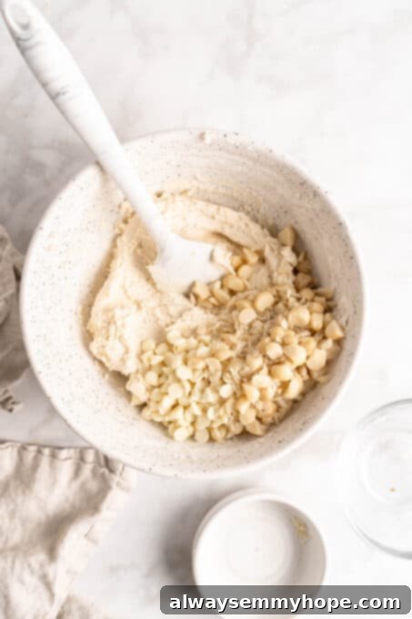 White chocolate chips and macadamia nuts folded into vegan cookie dough. Overhead view of creamy vegan cookie dough with a generous amount of white chocolate chips and perfectly chopped macadamia nuts folded in, ready for chilling.