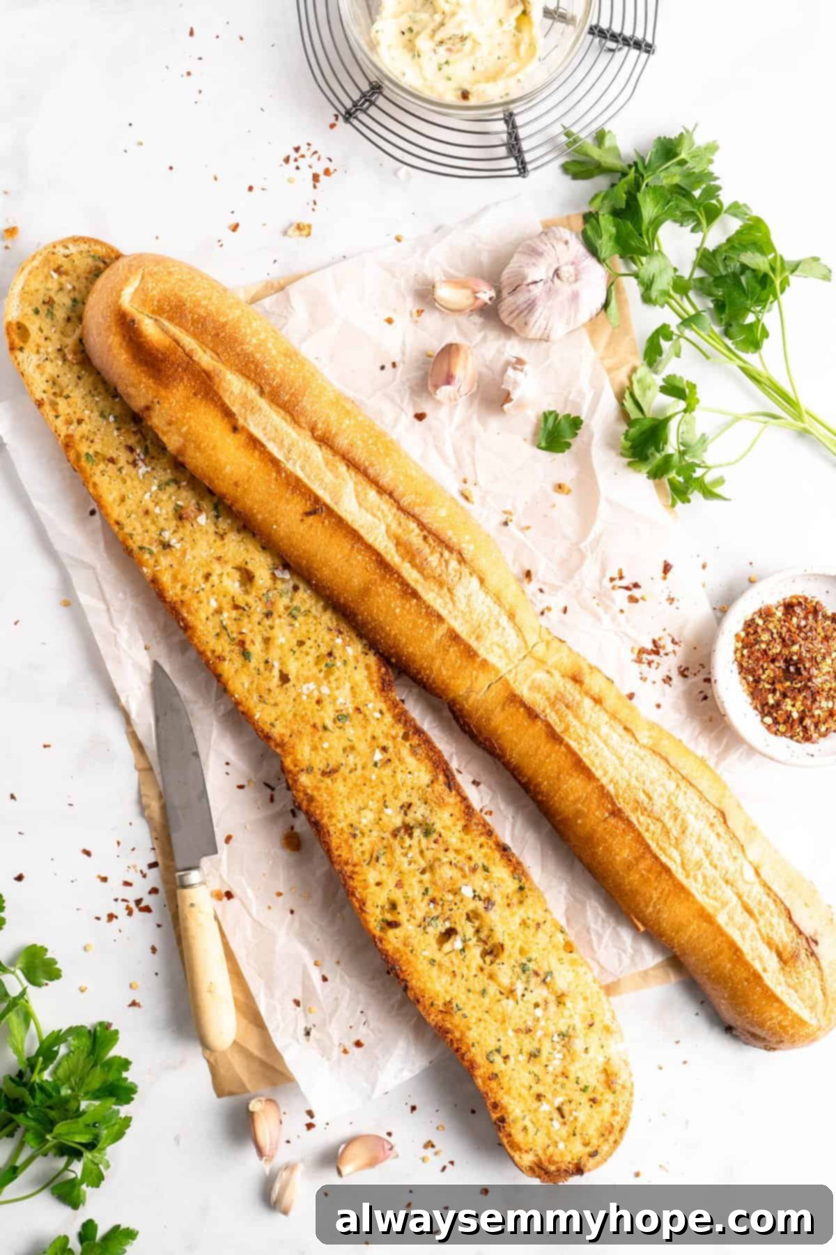 Two garlic bread halves surrounded by roasted garlic cloves, red pepper flakes, and fresh parsley, ready to be enjoyed