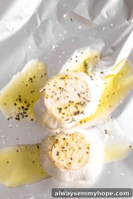 Two garlic heads cut open and drizzled with oil and salt on foil, ready for roasting