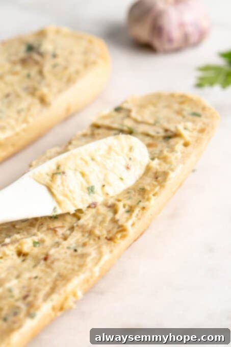 Hand smearing garlic butter onto a sliced baguette half on a baking sheet