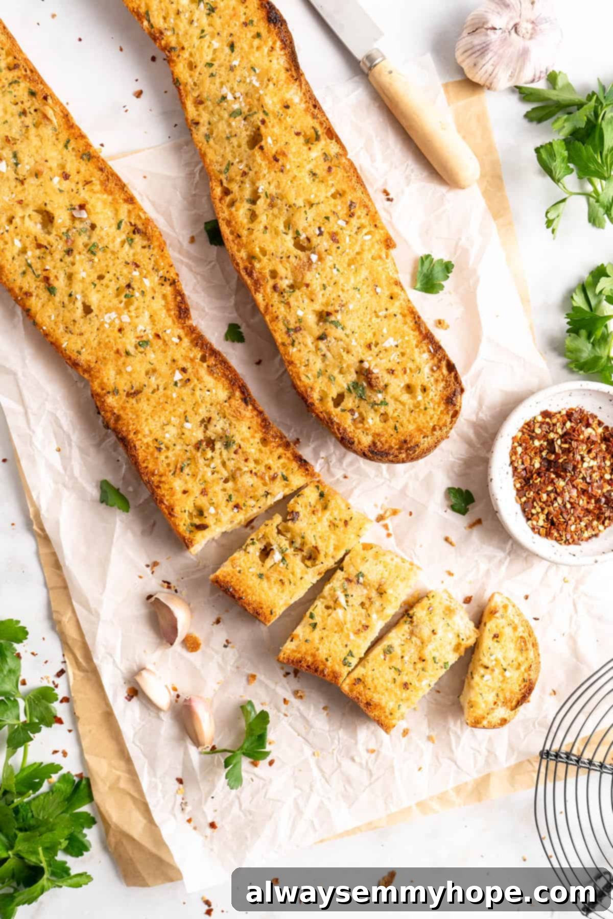 Two garlic bread halves on parchment paper, one partially sliced, showing the fluffy interior and golden crust