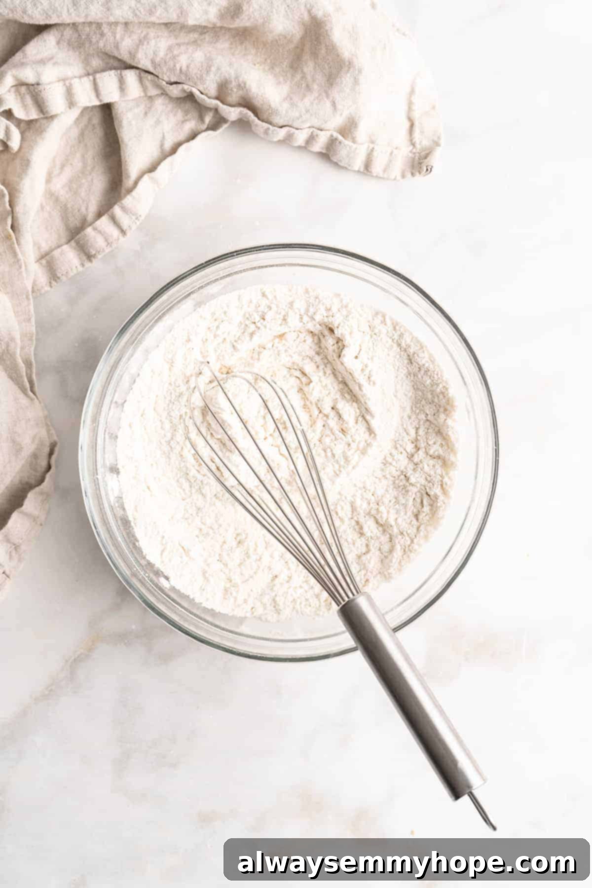 Plant-Based Chocolate Chip Bliss 6 Overhead view of dry ingredients, including all-purpose flour, cornstarch, baking soda, and sea salt, whisked together in a glass bowl, prepared for combining with wet ingredients for vegan chocolate chip cookies.