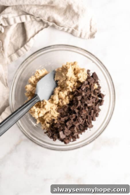 Plant-Based Chocolate Chip Bliss 8 Close-up overhead view of newly mixed vegan cookie dough in a glass bowl, with vegan chocolate chunks ready to be folded in with a spatula.