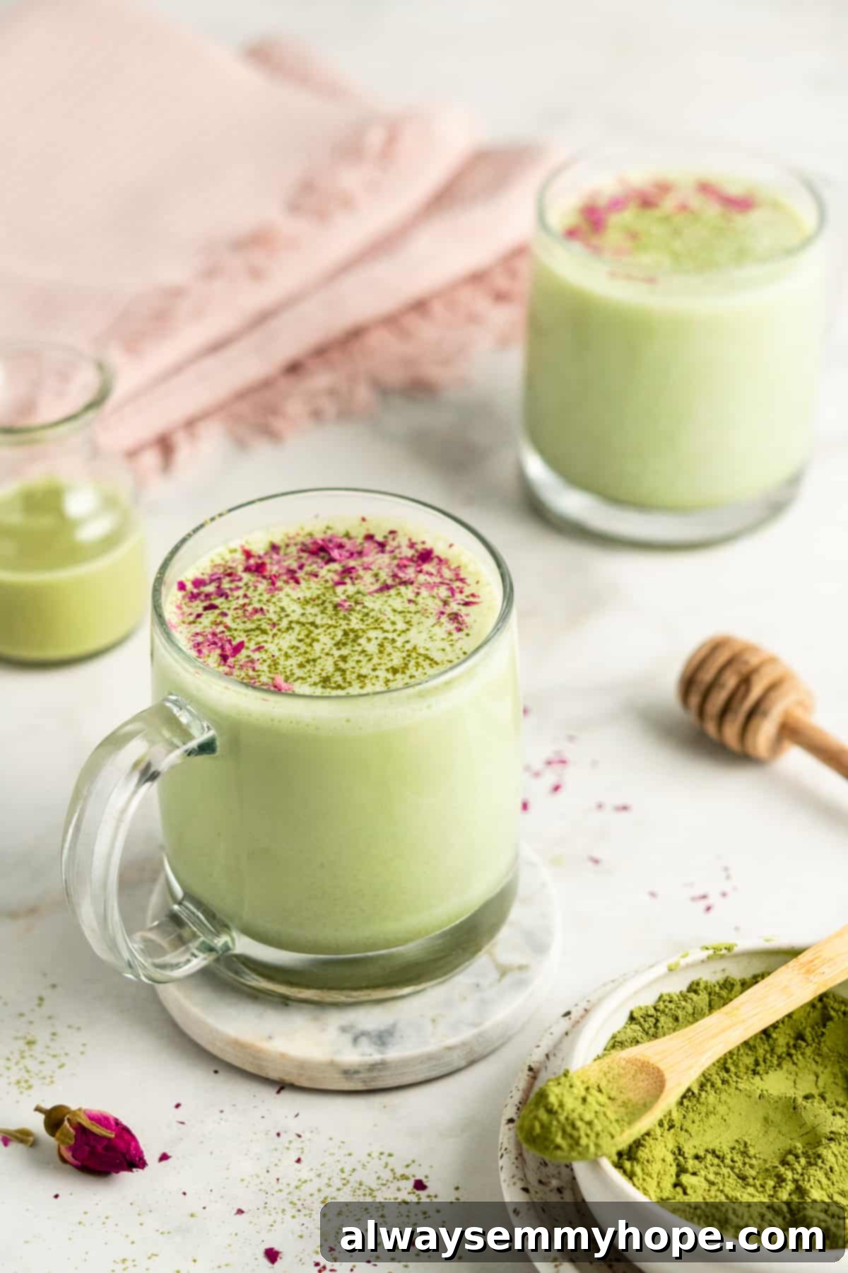 Two mugs of creamy hot matcha latte garnished with ground rose petals and a dusting of matcha powder, ready to be enjoyed.