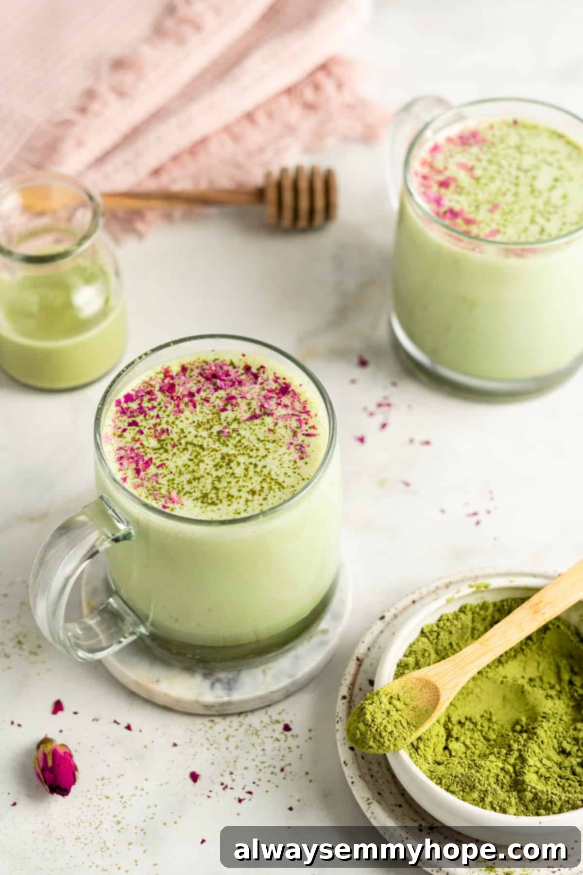 Two elegant glass mugs of steaming matcha latte, with a traditional white bowl of matcha powder in the foreground, creating a warm and inviting scene.