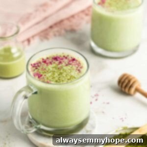 Two mugs of matcha latte garnished with ground rose petals and matcha powder