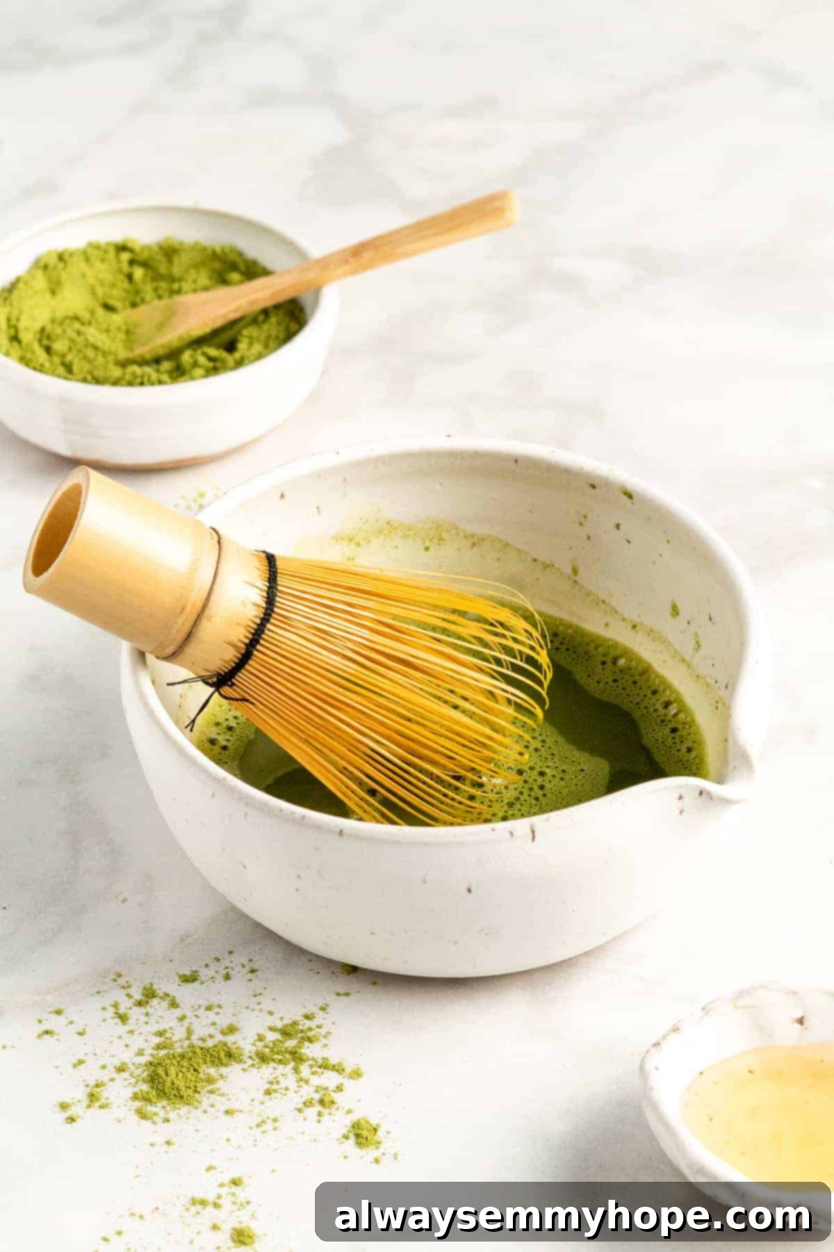 A traditional bamboo matcha whisk (chasen) standing upright in a small white bowl containing a vibrant green mixture of matcha and a small amount of hot water.
