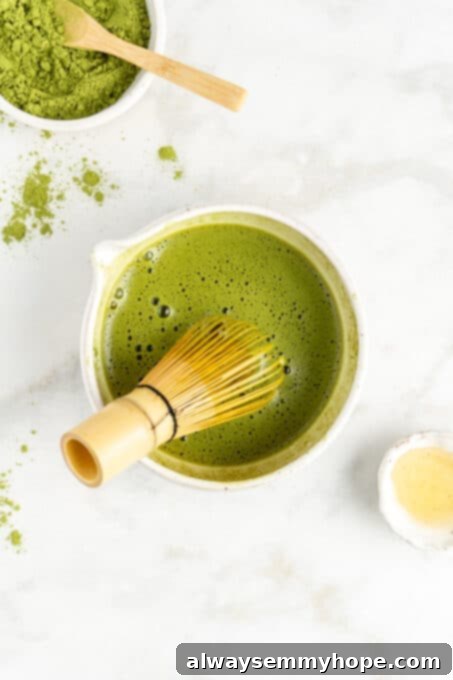 An overhead view of a bamboo matcha whisk actively whisking a bright green matcha mixture in a white bowl, creating a smooth and frothy consistency.