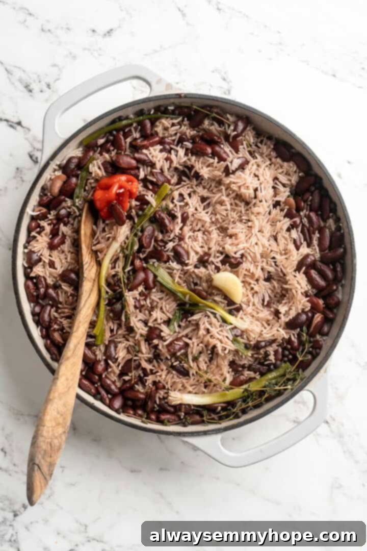 This authentic Jamaican rice and peas recipe is an easy side dish with lots of island vibes! It's packed with flavour and so simple to make. A wooden spoon gently stirring a pan of Jamaican rice and peas as it cooks, showcasing the blending of flavors and textures.