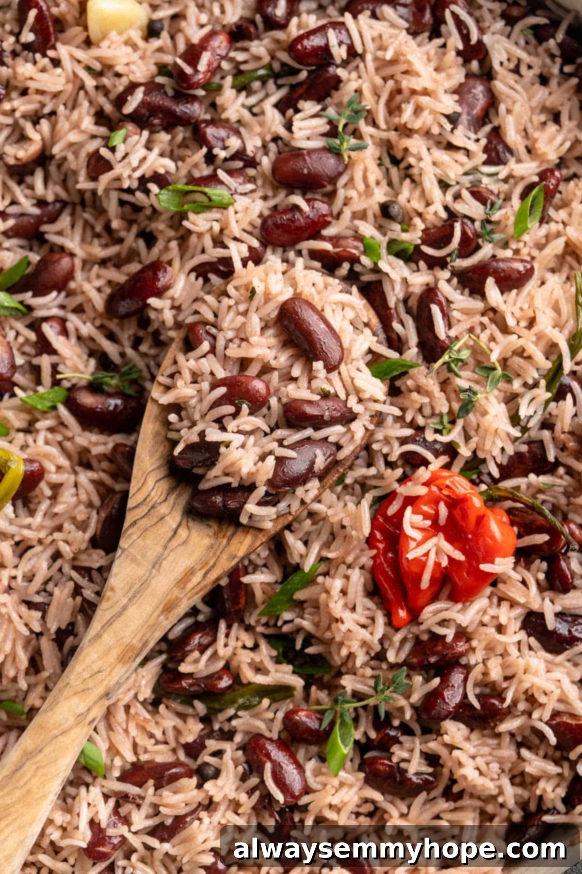 This authentic Jamaican rice and peas recipe is an easy side dish with lots of island vibes! It's packed with flavour and so simple to make. A wooden spoon rests in a pan of fluffy, perfectly cooked Jamaican rice and peas, inviting a taste.