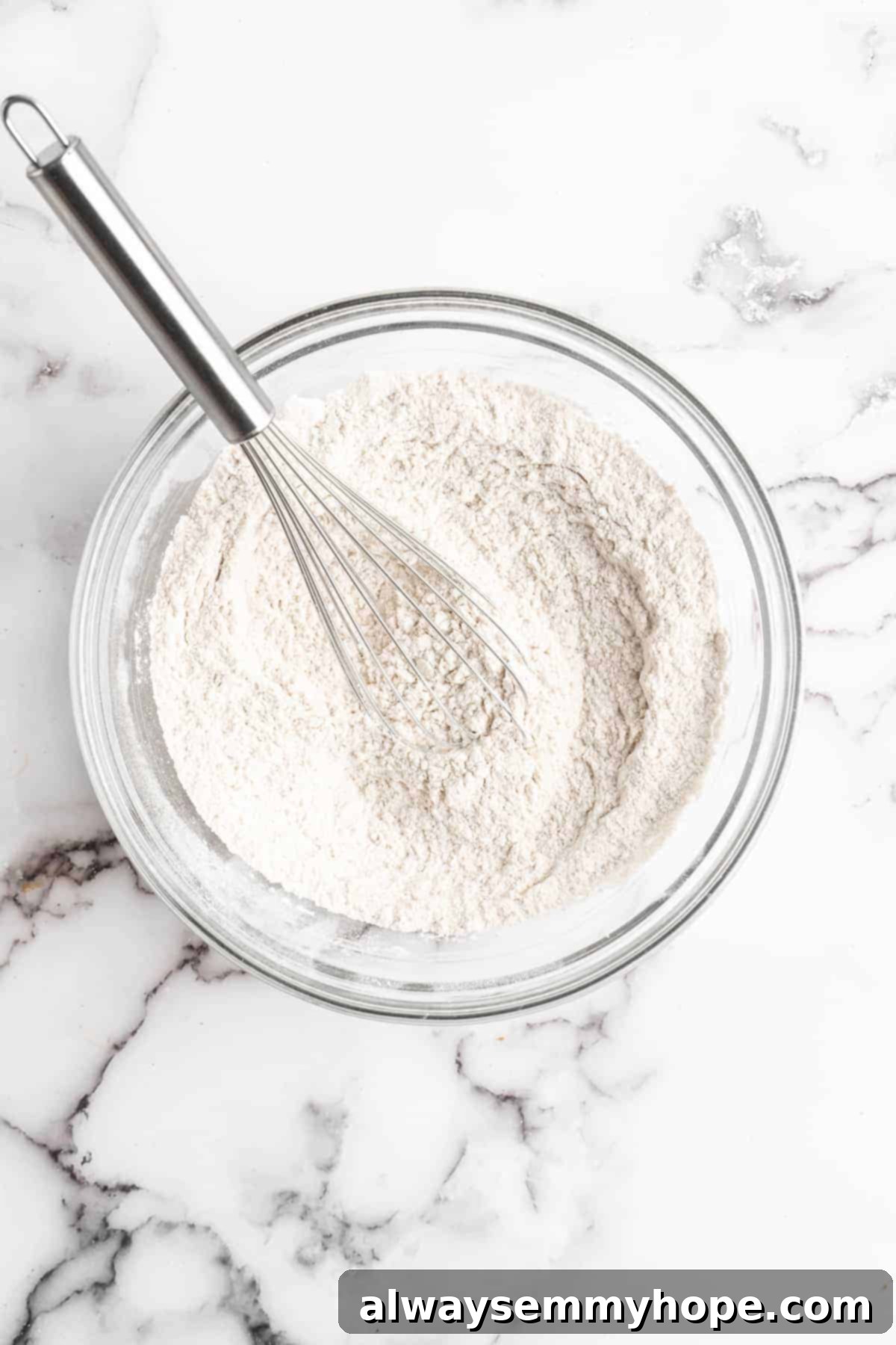 Dry ingredients in glass mixing bowl with whisk