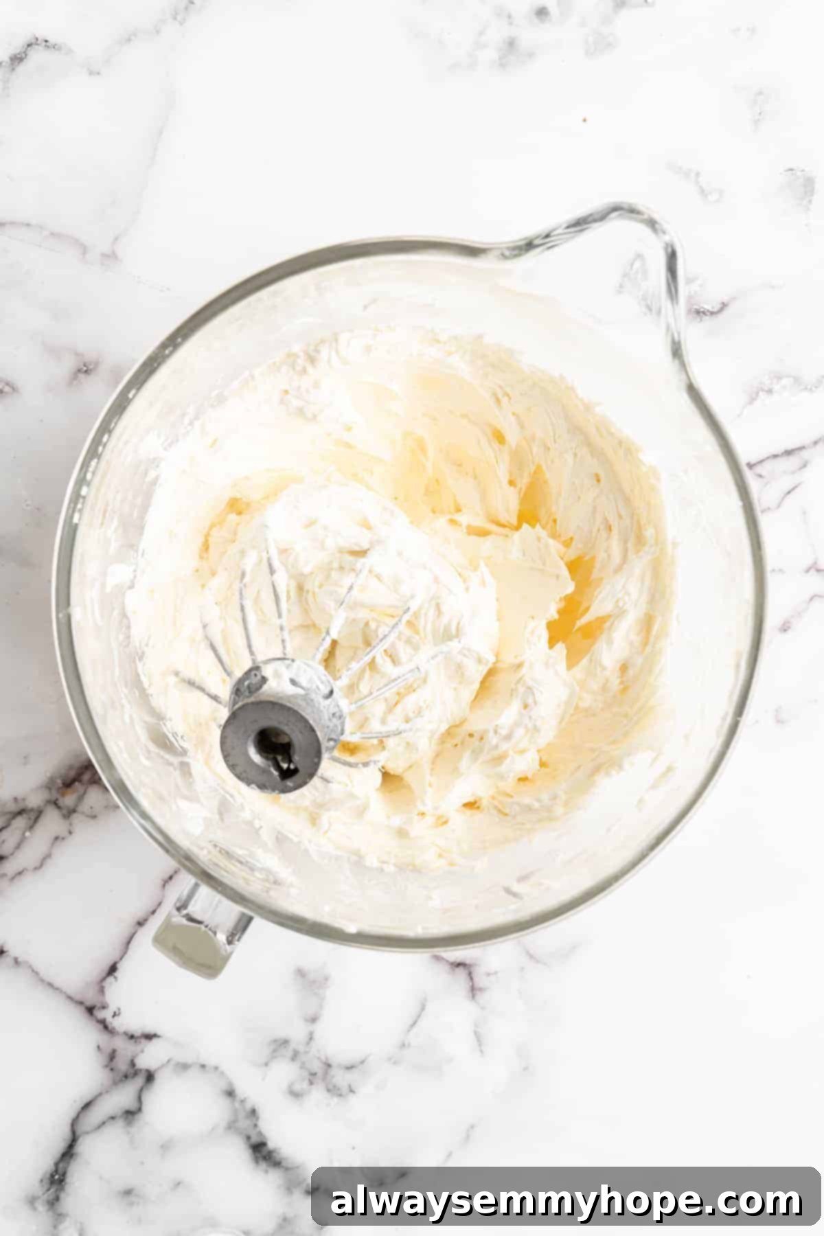 Vegan cream cheese and butter in glass mixing bowl with whisk attachment