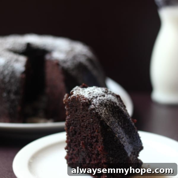 A close-up view of a slice of rich Guinness Chocolate Cake on a white plate, revealing its delicate crumb and inviting texture, lightly dusted with powdered sugar.