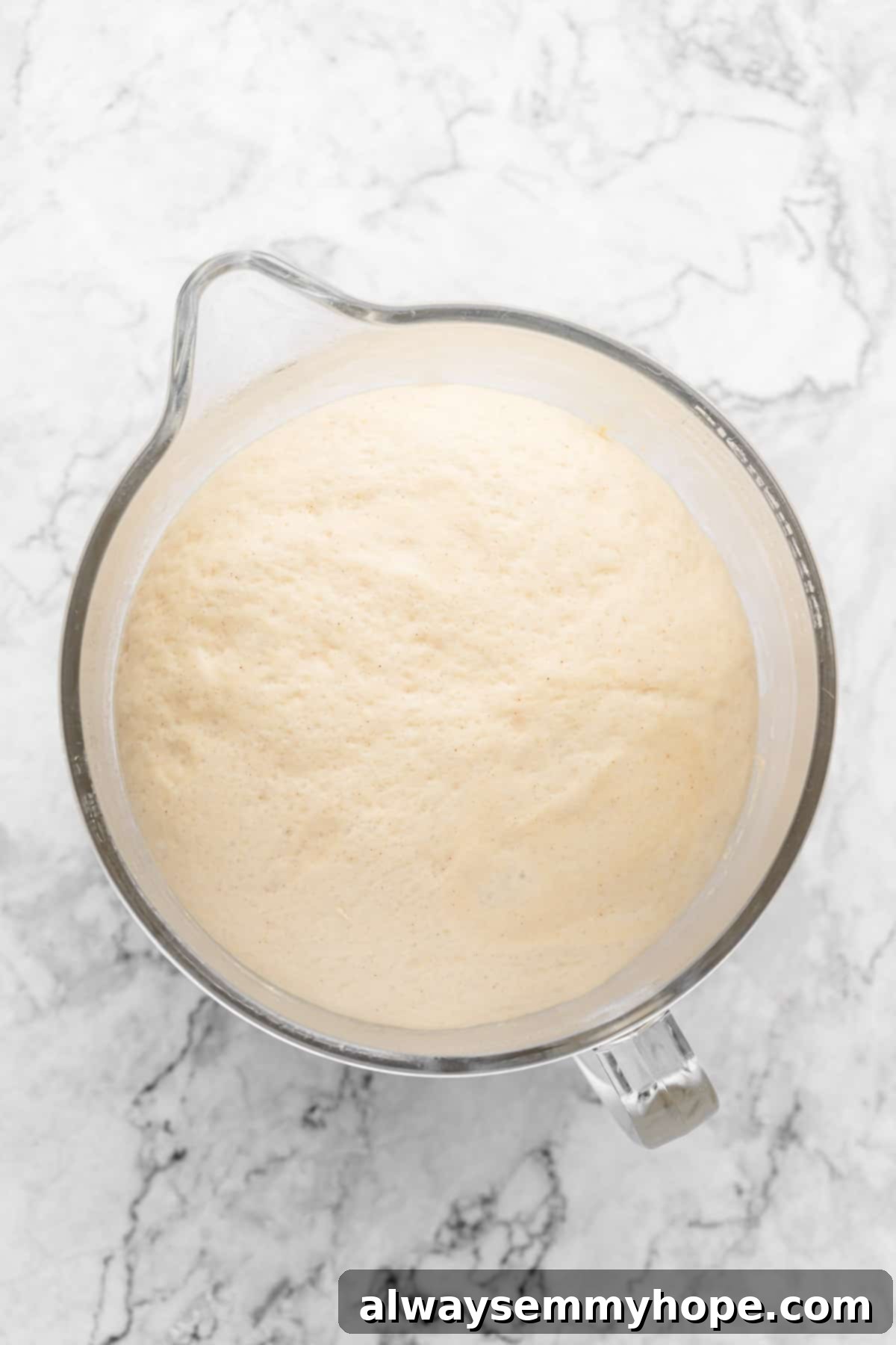 Overhead view of cinnamon roll dough in a glass mixing bowl after it has risen and doubled in size.