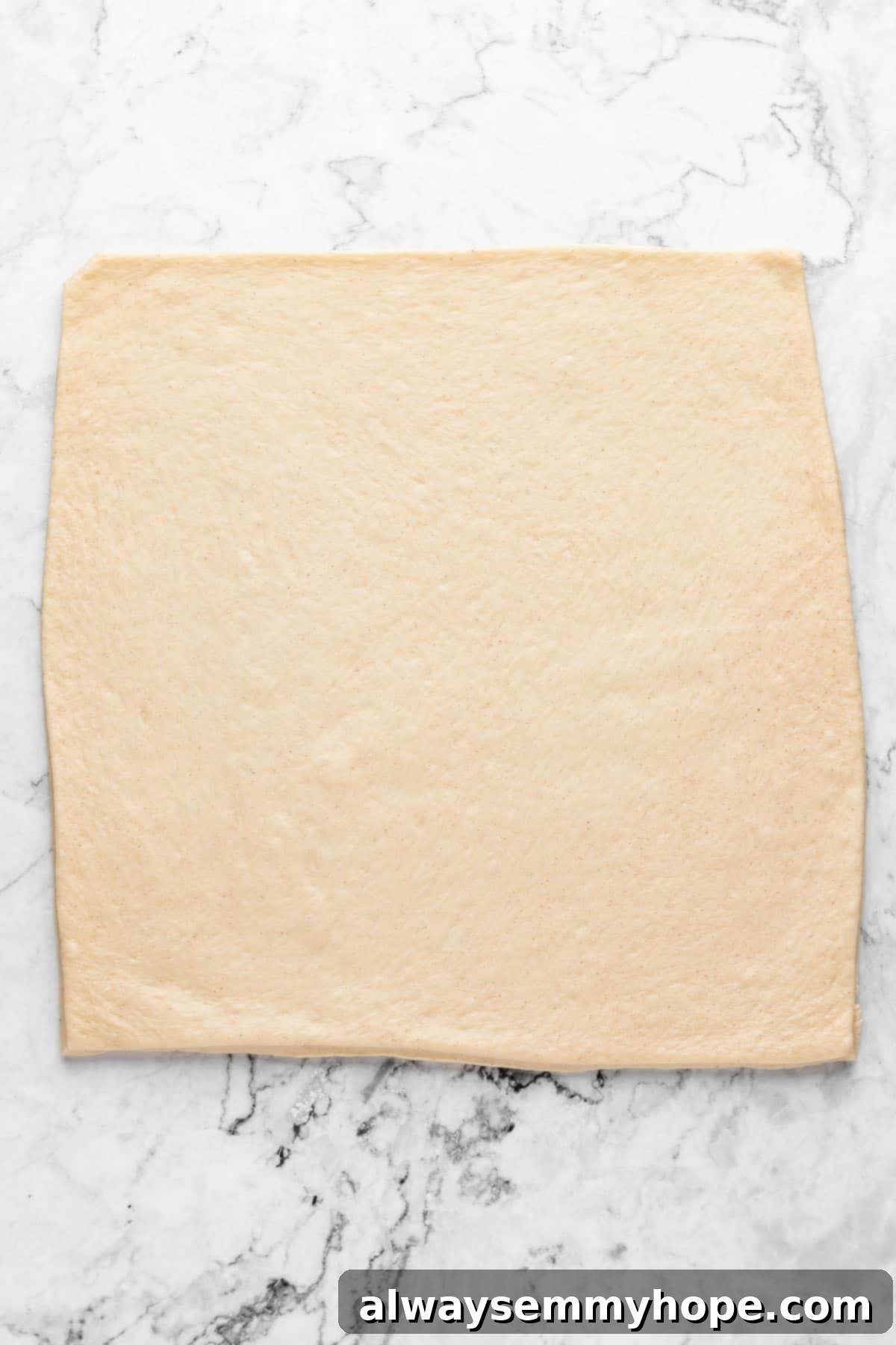 Overhead view of rolled out cinnamon roll dough on a floured surface, forming a 12x12 inch square.