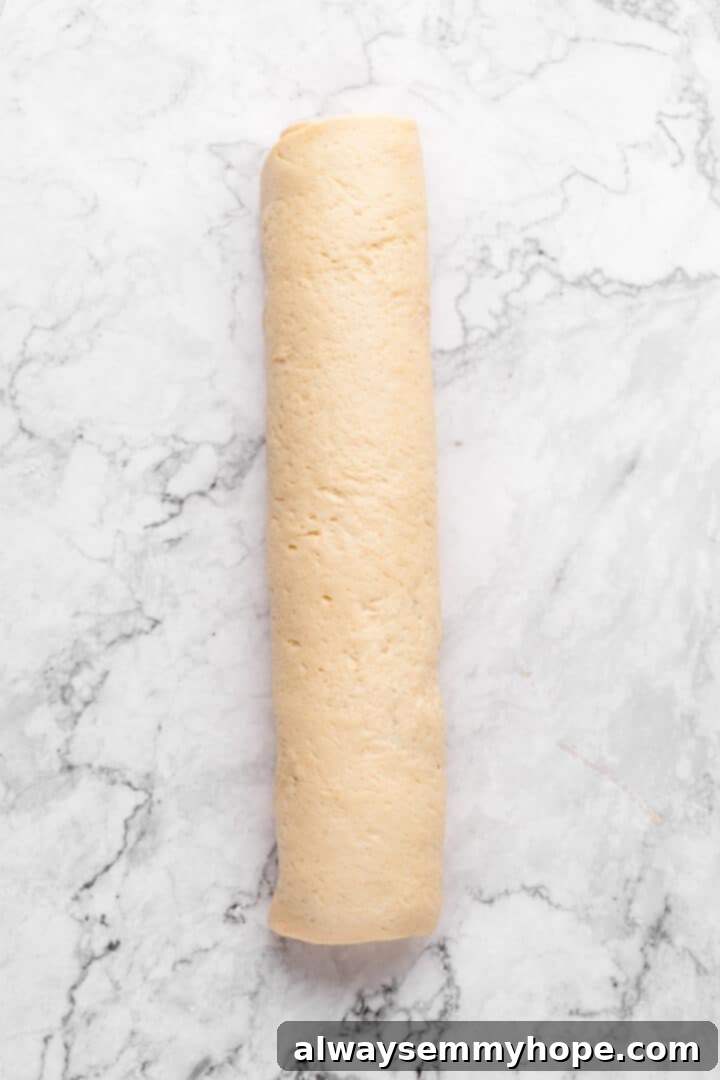 Overhead view of the cinnamon roll dough rolled tightly into a log shape with filling visible.