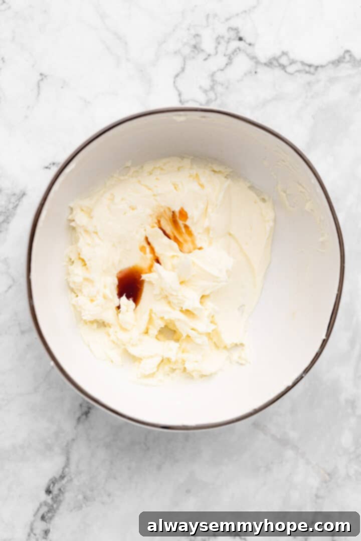 Overhead view of vanilla extract being added to creamed vegan butter and cream cheese in a mixing bowl.