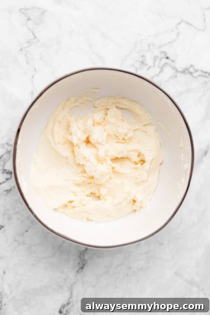 Overhead view of creamed vegan butter, cream cheese, and vanilla in a mixing bowl, prior to adding powdered sugar.