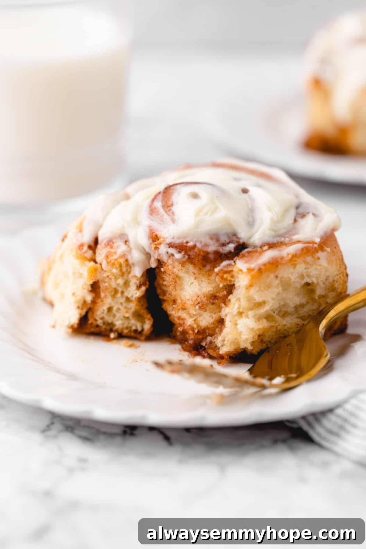 A close-up of a vegan cinnamon roll on a plate, with a corner gently torn off to reveal the fluffy interior and cinnamon swirl.
