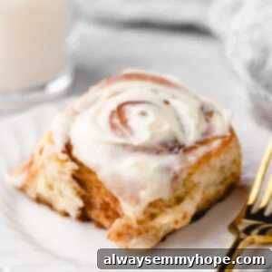 Vegan cinnamon roll on white plate with gold fork, with glass of milk in background