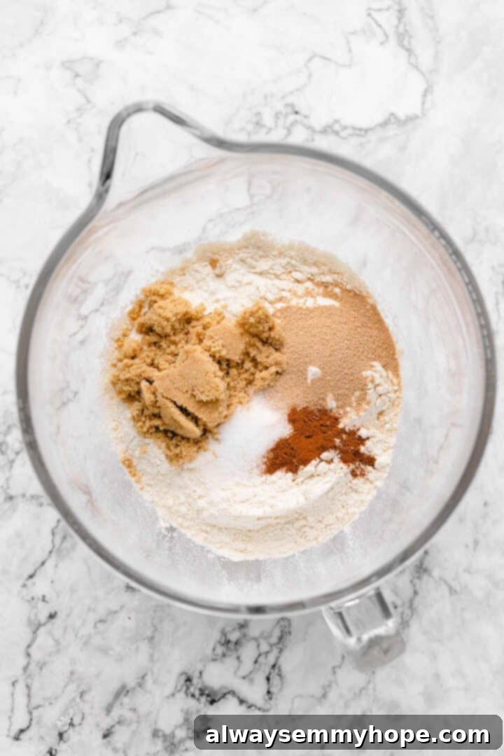 Overhead view of dry ingredients for cinnamon roll dough in a glass mixing bowl: bread flour, sugar, yeast, salt, and cinnamon.