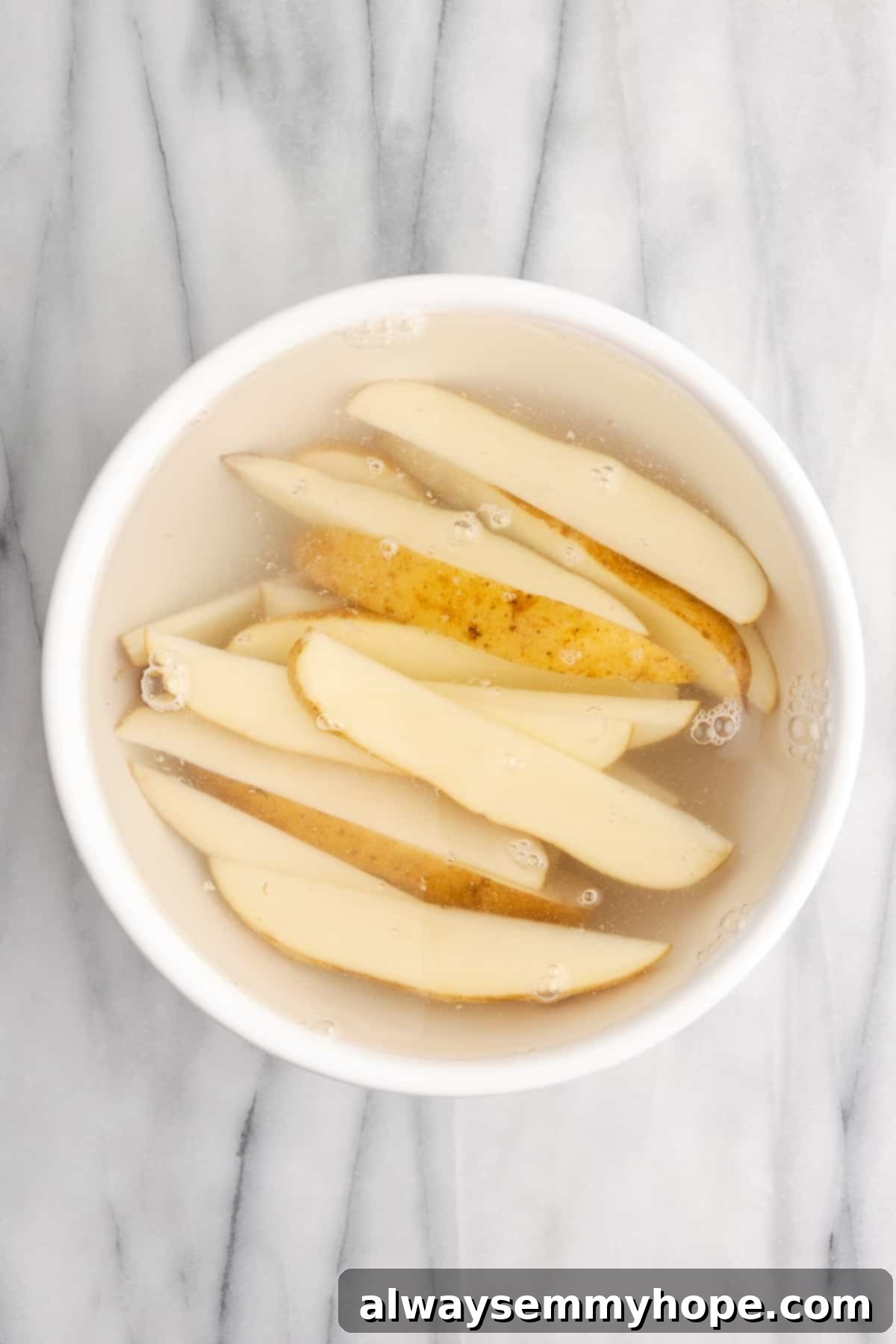 These quick and easy air fryer potato wedges are crispy on the outside, fluffy on the inside, and the perfect side for your burger. Uncooked potato wedges meticulously soaking in a large bowl of cold water, a critical preparatory step that extracts excess starch to ensure maximum crispiness when air-fried.