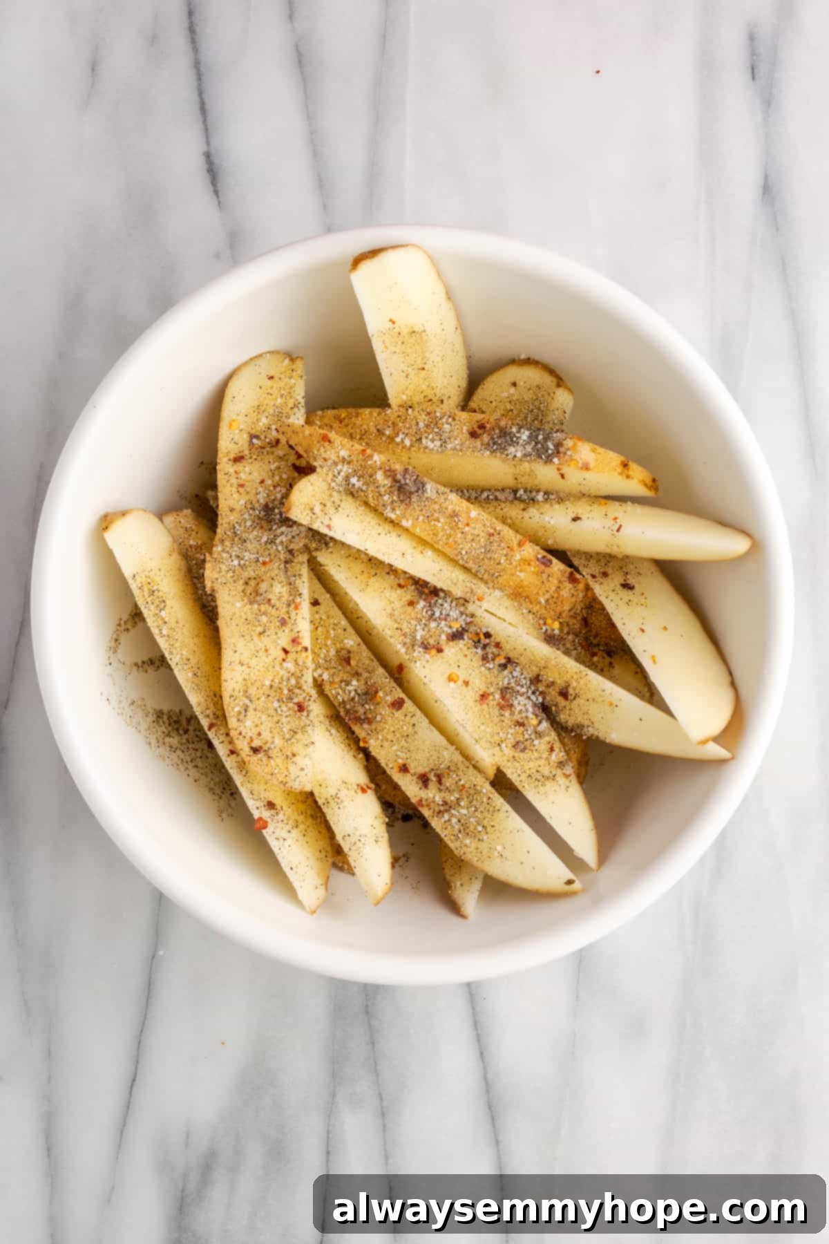 These quick and easy air fryer potato wedges are crispy on the outside, fluffy on the inside, and the perfect side for your burger. Uncooked potato wedges in a mixing bowl, generously coated with olive oil and a vibrant array of seasonings, ready to be tossed and air-fried to crispy perfection.