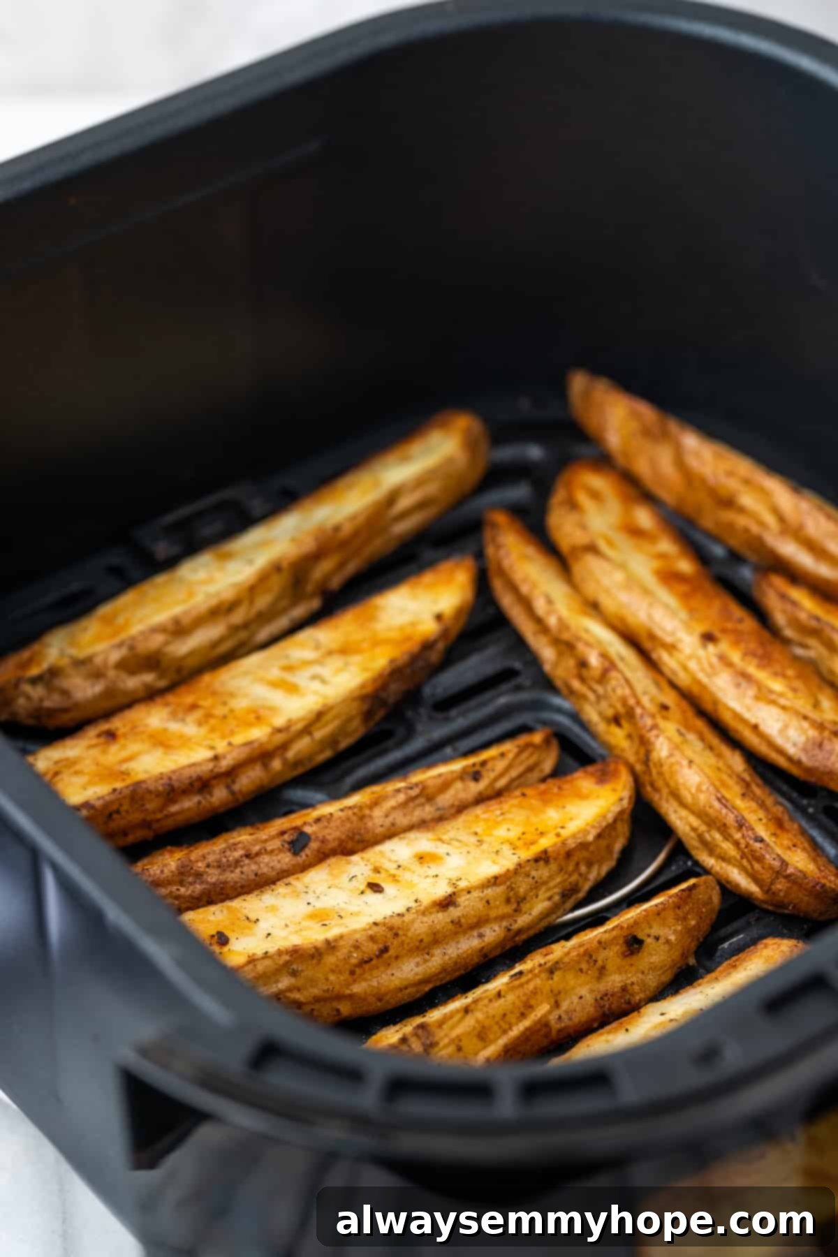 These quick and easy air fryer potato wedges are crispy on the outside, fluffy on the inside, and the perfect side for your burger. Golden-brown, perfectly cooked air fryer potato wedges, hot and crispy, resting in the air fryer basket after being tossed halfway through the cooking process.