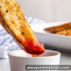 Crispy Air Fryer Potato Wedges 2 A perfectly cooked air fryer potato wedge being dipped into a small bowl of vibrant red ketchup, emphasizing its crispy texture and delicious appeal.